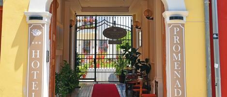 A hotel entrance with a red carpet, a gate, and a sign that reads "PROMENADE HOTEL".