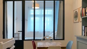 A room with a wooden table, two chairs, a bookshelf, and a window with curtains.