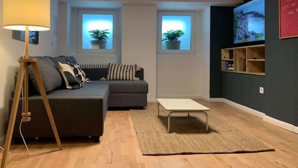 A modern living room with a sectional sofa, a floor lamp, a coffee table, and a TV on a dark wall.
