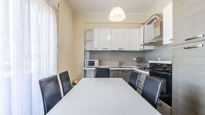A modern kitchen with white cabinets, a microwave, a stove, and a dining table with chairs. - Spacious Stay in the Heart of Tirana 2BR City View (Tirana)