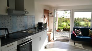 Cocina moderna con horno empotrado, cafetera y lavaplatos. Hay una puerta corrediza de vidrio que da a un jardín con plantas y un sofá azul.