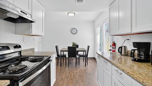 A modern kitchen with white cabinets, a stainless steel stove, a dining table with chairs, and a coffee maker. - Bright 2Bd 1Bt Homes in Central Wellington (College Park)