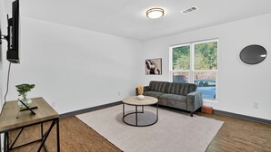 A modern living room with a sofa, a coffee table, a TV, and a large window with blinds. - Bright 2Bd 1Bt Homes in Central Wellington (College Park)