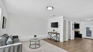 A modern living room with a grey sofa, a round coffee table, and a flat-screen TV mounted on the wall. - Bright, Spacious 2Bd 2.5Bt Townhome Interior (College Park)
