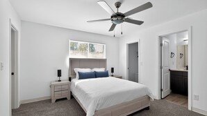 A bedroom with a bed, a ceiling fan, a nightstand, a window, and a door leading to a bathroom. - Bright, Spacious 2Bd 2.5Bt Townhome Interior (College Park)