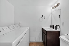 A modern bathroom with a white sink, dark wooden cabinet, and a mirror with lights. - Bright, Spacious 2Bd 2.5Bt Townhome Interior (College Park)