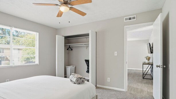 Un dormitorio con cama, ventilador de techo, armario y puerta que da a otra habitación.