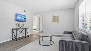 Una sala de estar moderna con un sofá gris, una mesa de centro redonda y un televisor de pantalla plana montado en la pared.