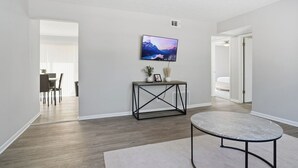 Una sala de estar moderna con un televisor de pantalla plana montado en la pared, una mesa redonda de centro y una consola con objetos decorativos.