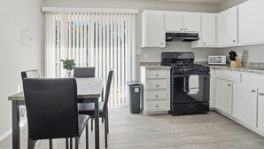 Una cocina moderna con armarios blancos, una estufa negra y una zona de comedor con mesa y sillas.