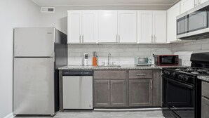 Una cocina moderna con armarios blancos, un refrigerador de acero inoxidable, un lavavajillas, un microondas y una estufa negra.