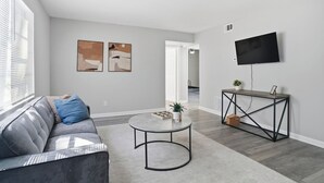 Una sala de estar moderna con un sofá gris, una mesita redonda y un televisor en la pared.