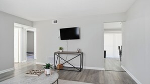 Una sala de estar moderna con un televisor de pantalla plana montado en la pared, una mesa de centro redonda y una mesita auxiliar con una planta.