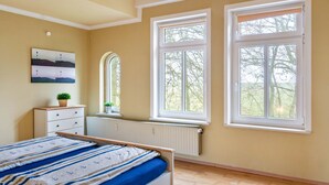 A bedroom with a bed, dresser, radiator, and large windows. - Apartment 'Villa Am Alten Deich' with Shared Terrace, Shared Garden and Wi-Fi (Butjadingen)