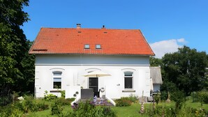 A white building with a red roof, a covered entrance, and a garden with various plants. - Apartment 'Villa Am Alten Deich' with Shared Terrace, Shared Garden and Wi-Fi (Butjadingen)