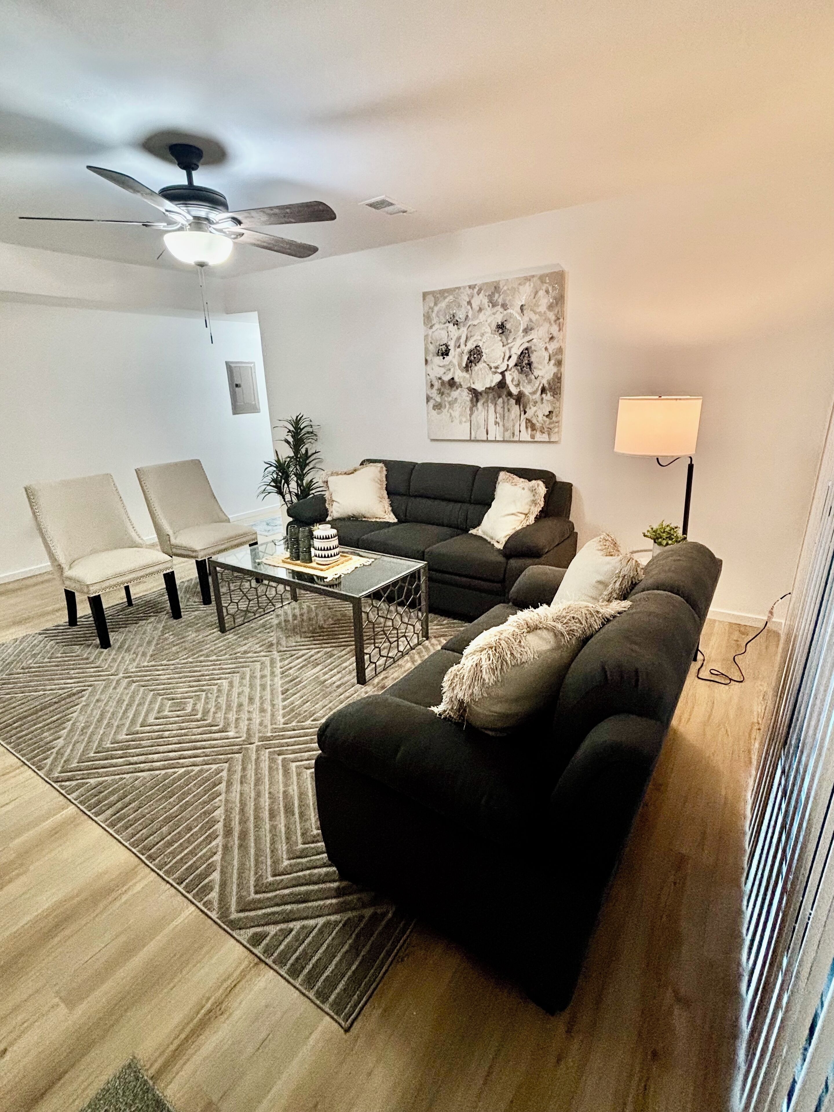 Un salon moderne avec un canapé vert foncé, deux fauteuils beige, une table basse et un ventilateur de plafond.
