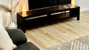 Un salon moderne avec un téléviseur à écran plat posé sur un meuble noir, une horloge murale et un tableau encadré au-dessus du téléviseur.