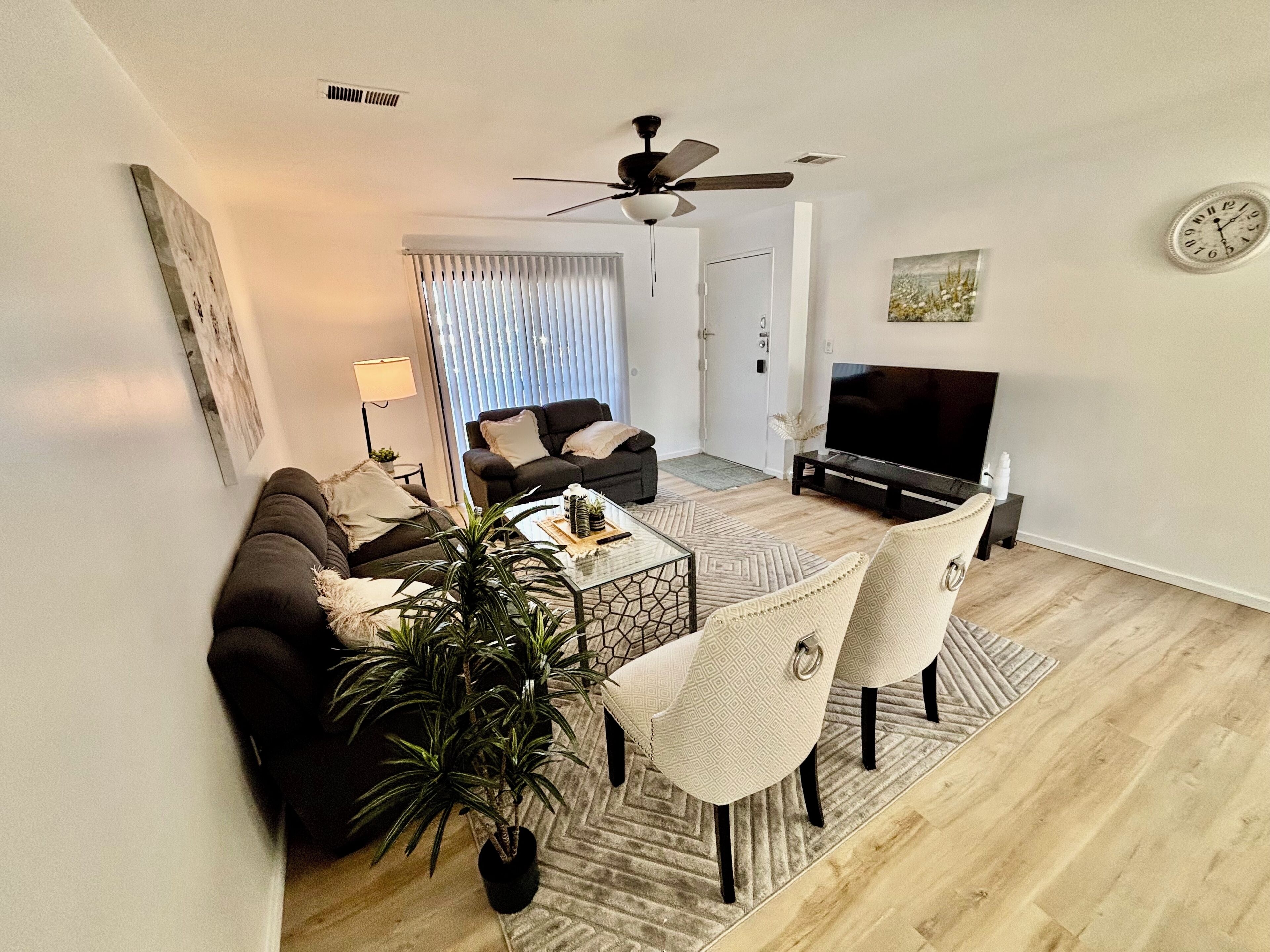 Een woonkamer met een bank, stoelen, een salontafel, een televisie en een plafondventilator.