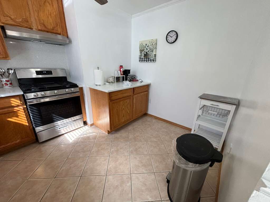 A kitchen with a stainless steel stove, wooden cabinets, a trash can, and a wall-mounted clock.