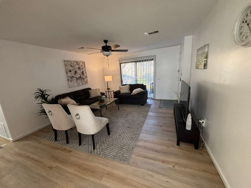 A living room with a ceiling fan, two sofas, a dining table with chairs, and a TV stand.