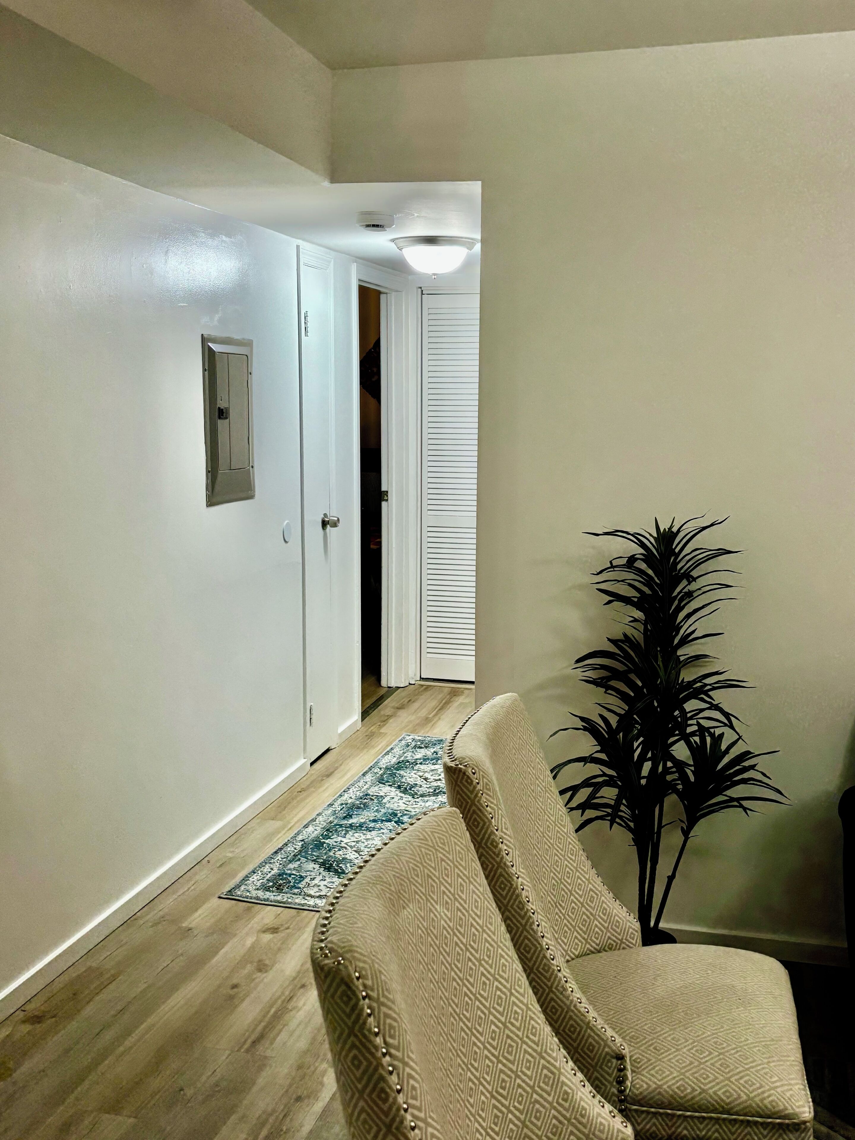 A hallway with a beige patterned armchair, a potted plant, and a wooden floor.