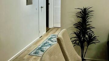 A hallway with a beige patterned armchair, a potted plant, and a wooden floor.