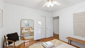 Ein Schlafzimmer mit Bett, Sessel, Deckenventilator, Kleiderschrank und Wandteppich.