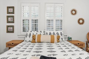 Ein Schlafzimmer mit einem Bett, zwei Nachttischen, einem Fenster mit Jalousien und Wanddekorationen.
