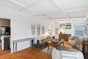Ein modernes Wohnzimmer mit Sofa, Couchtisch und Sessel, ein Essbereich mit einer Bank und eine Küche mit Herd.