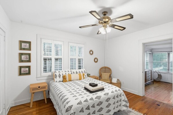 A bedroom with a bed, a ceiling fan, a window, a chair, and a small table.
