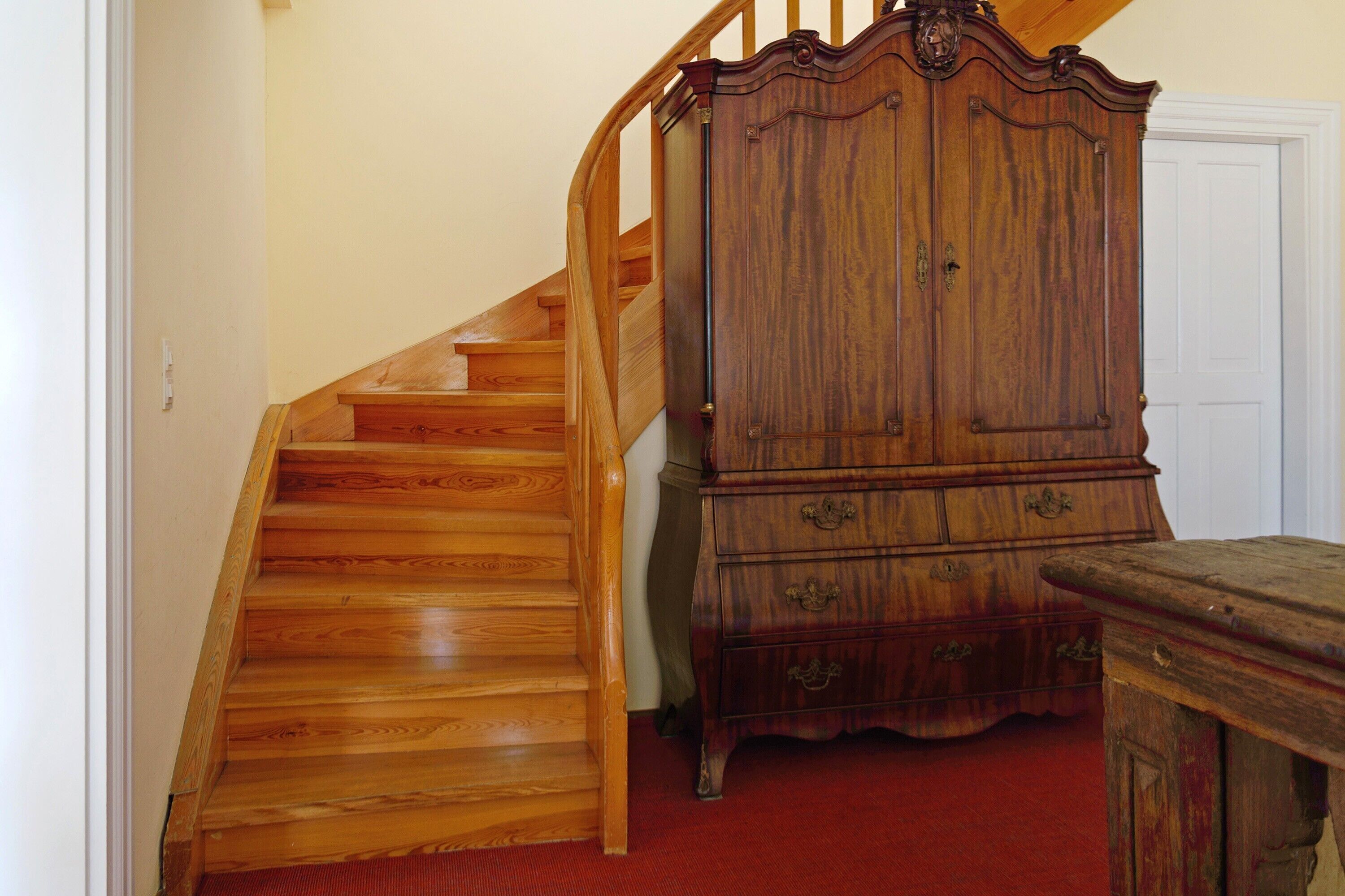 Una scala in legno conduce a un pianerottolo con un armadietto e una porta sullo sfondo.