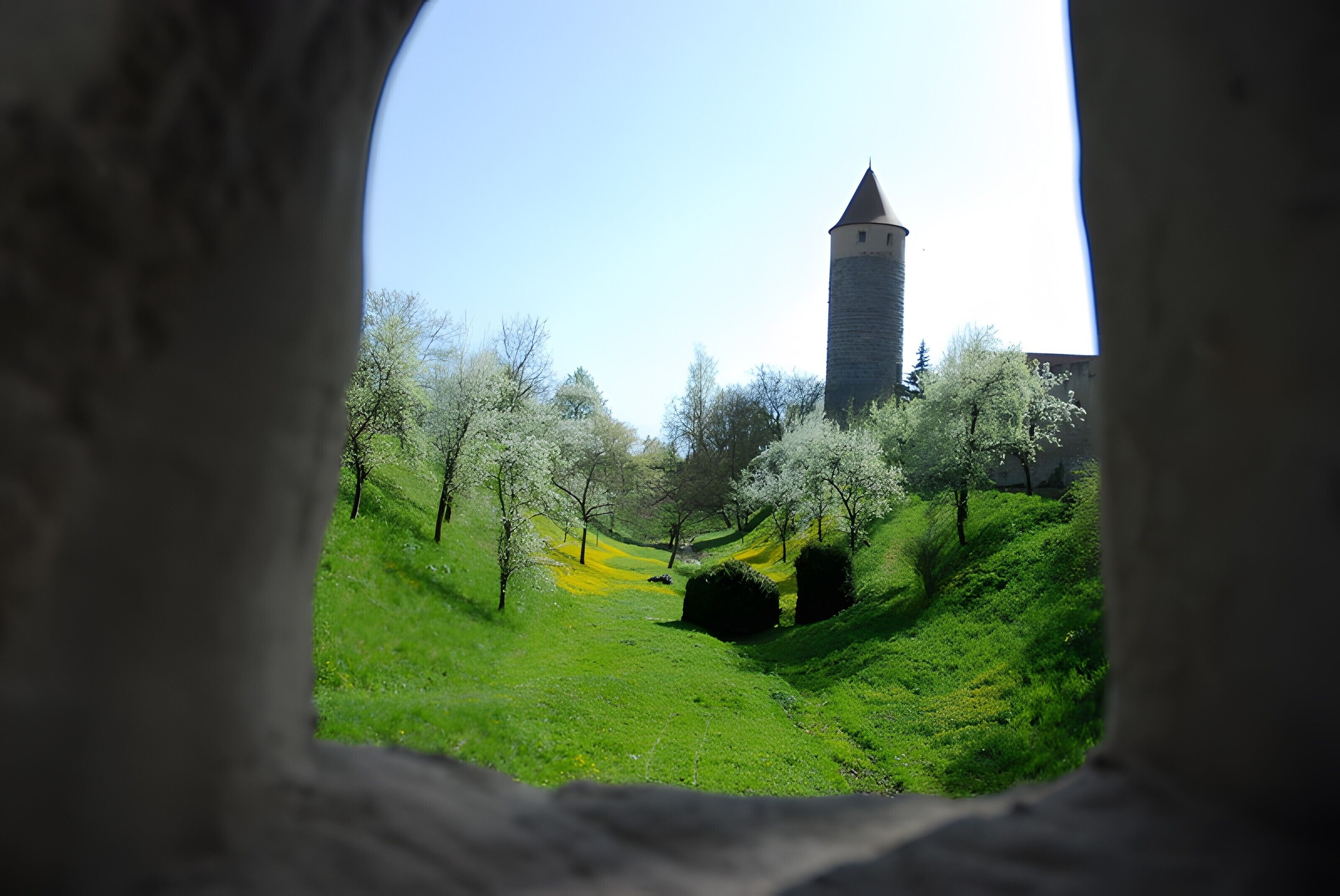 Une vue à travers une fenêtre sur un paysage verdoyant avec une tour en pierre.