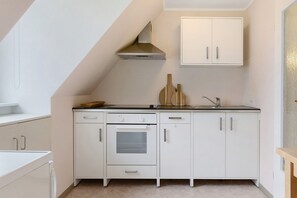 Une cuisine avec des meubles blancs, une hotte de cuisinière en acier inoxydable, un four, un évier et une planche à découper en bois.