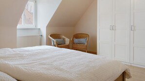 A bedroom with a large bed, two wicker chairs, a white wardrobe, and a window with a view of a building. - Apartment 'Schwanbergblick' with Shared Garden and Wi-Fi (Iphofen)