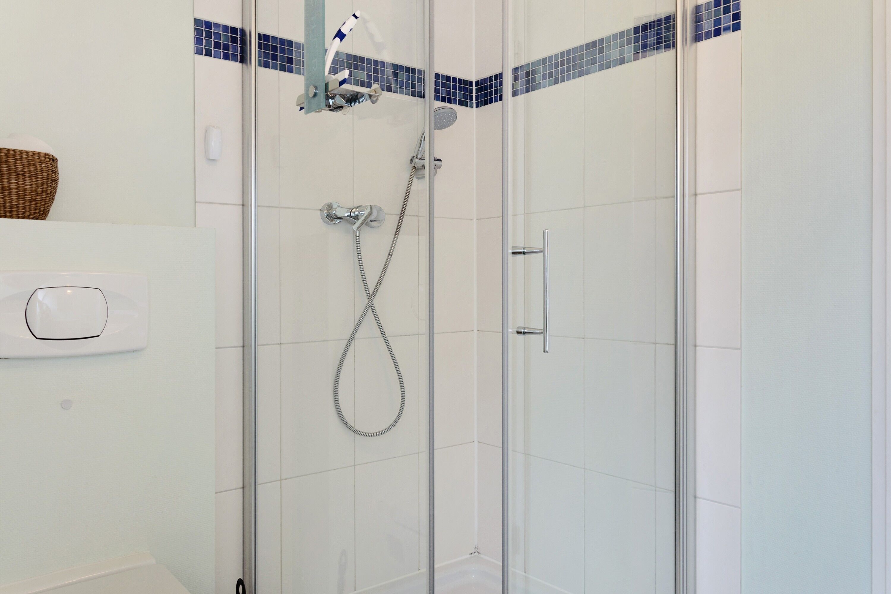 A glass-enclosed shower with a handheld showerhead and a wall-mounted faucet.