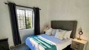 A bedroom with a bed, nightstand, lamp, and a window with curtains. - Cosy modern cottage only 10 minutes from the city centre (Mutare)
