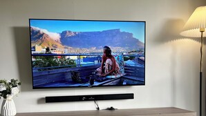 Un televisor de pantalla plana montado en la pared, un mueble bajo de madera y una mesa con dos vasos y un juego de mesa Monopoly.