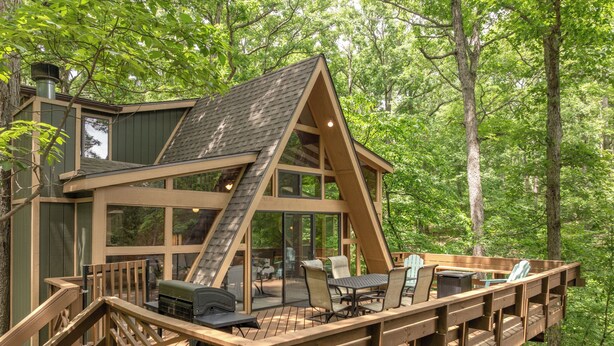 Une terrasse en bois avec des meubles d’extérieur, un escalier et une grande fenêtre donnant sur une forêt.