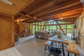 Interior de madera con comedor, sofá y ventanas amplias.
