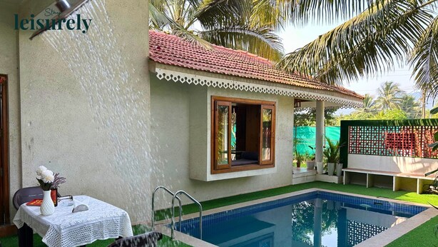 Zona de piscina con una casita, una mesa con un florero y una silla.