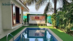 Una piscina con cubierta de madera, rodeada de césped artificial y palmeras.