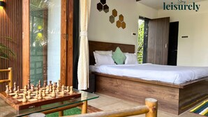 A modern bedroom with a wooden bed, a glass chess table, and a view of greenery outside. - Stay Leisurely Blue Leaf 3BHK Alibaug (Alibag)