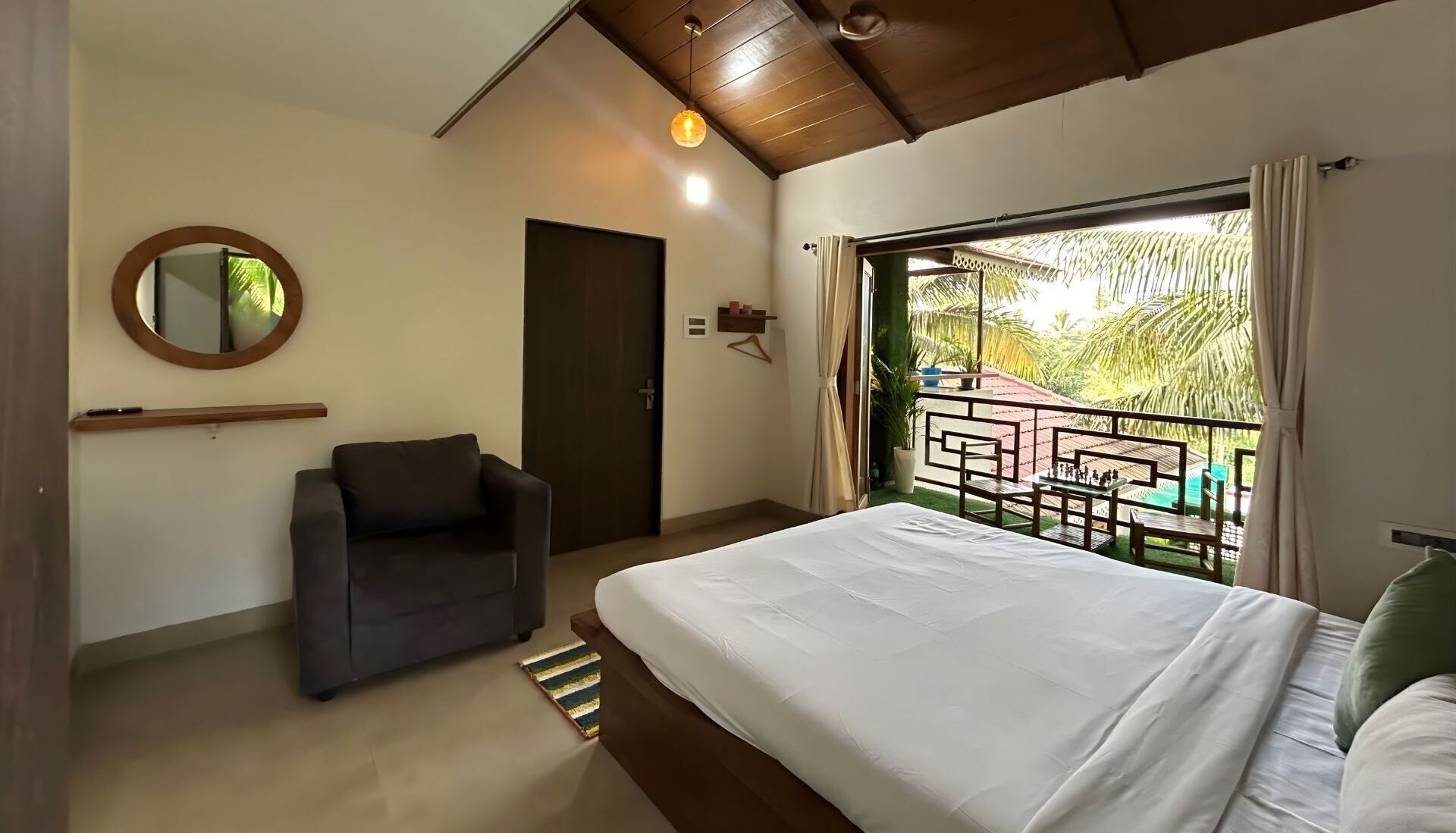 Une chambre avec un lit, une chaise, un miroir et un balcon donnant sur des palmiers.