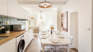 A modern kitchen with a built-in washing machine, a dining area with a table set for four, and a pendant light above the table. - Merveil Family Suite - Fbg St Antoine (Paris)