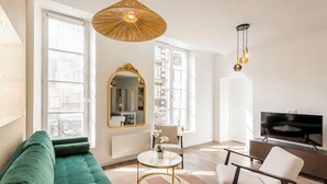 A modern living room with a green sofa, a round coffee table, a large mirror, and a TV on a wooden stand. - Merveil Family Suite - Fbg St Antoine (Paris)