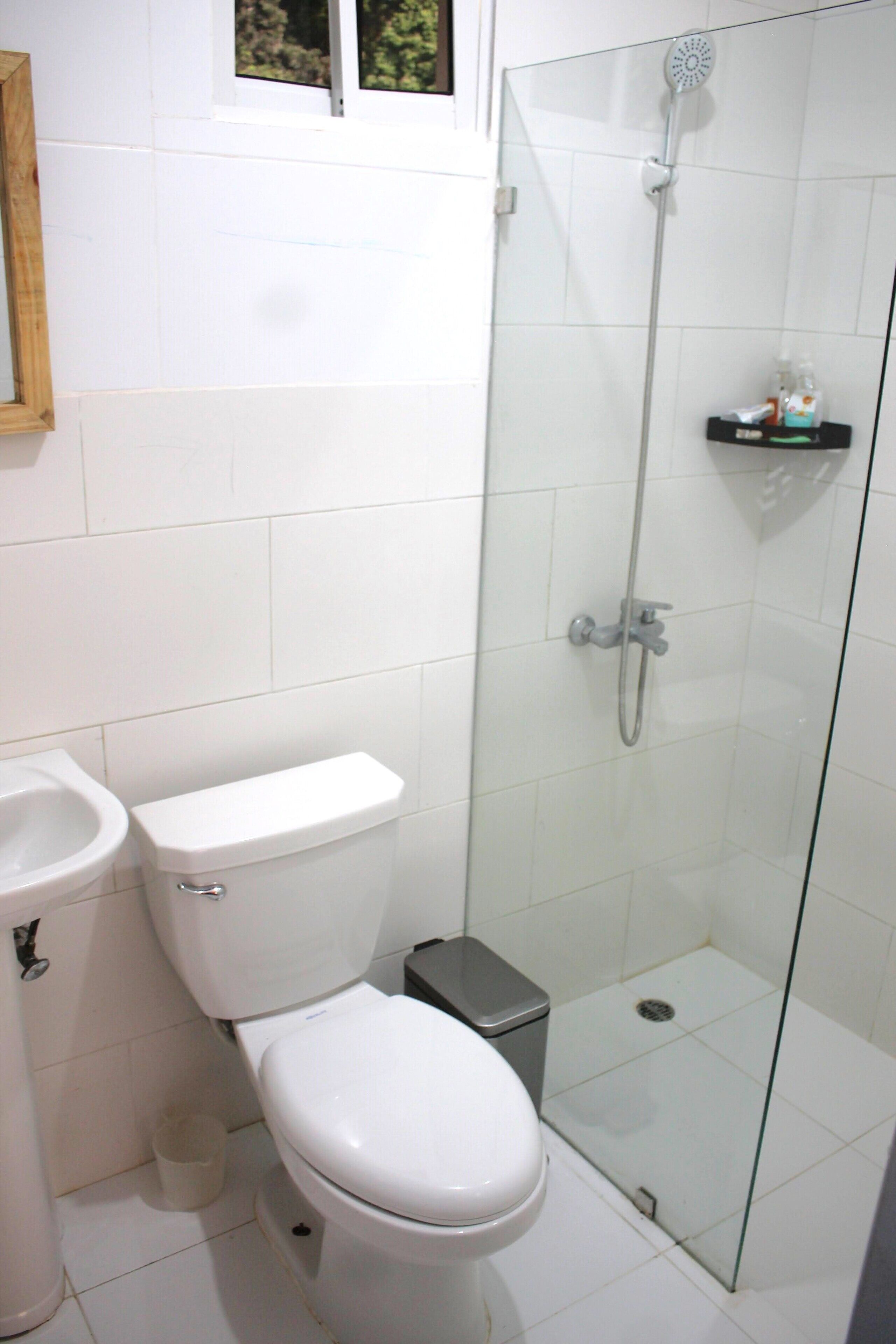 Et badeværelse med toilet, bidet og brusekabine med glasvægge.