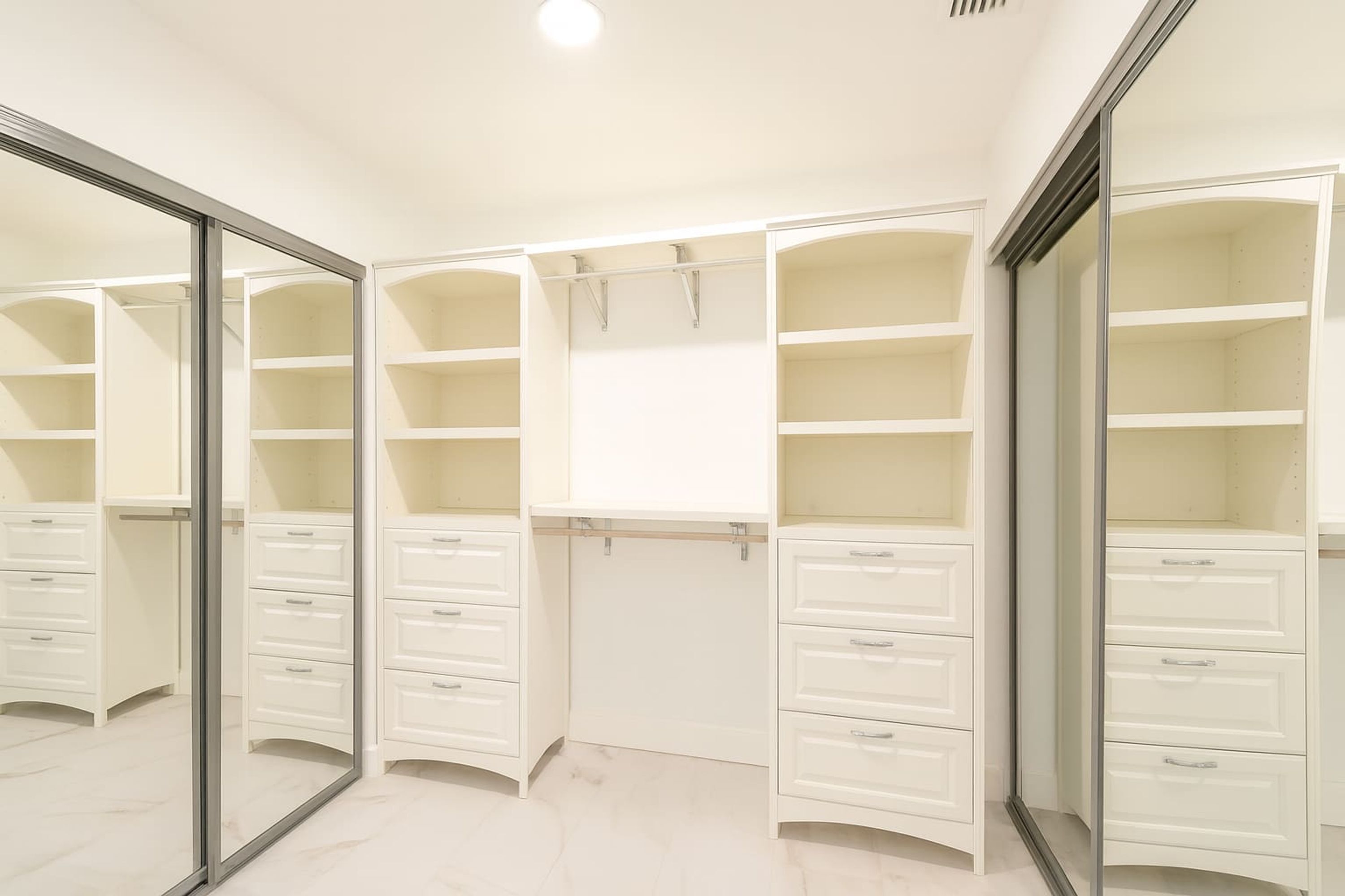 Ein begehbarer Kleiderschrank mit mehreren Regalen und Schubladen, einem Spiegel und einer Deckenleuchte.