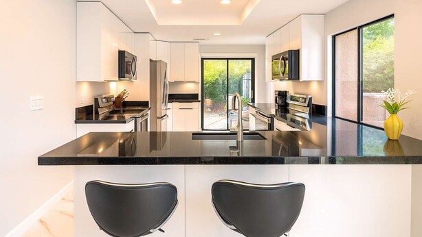 A modern kitchen with a central island, black bar stools, and a large window providing a view of the outdoors. - Modern Luxury at Ironwood Country Club Palm Desert (Palm Desert)