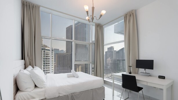 Een moderne hotelkamer met een groot bed, een bureau en uitzicht op hoge gebouwen door grote ramen.