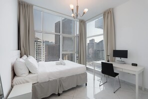 A modern hotel room with a large bed, a desk, and a view of tall buildings through large windows. - Stayshort - 2BR in Dubai Marina Sleeps 4 With Canal View (Dubai)